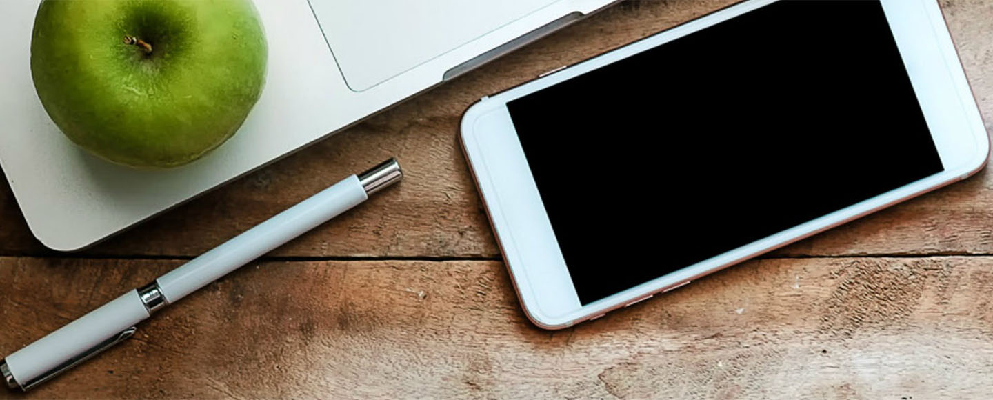 Mobile phone, pen and green apple on a wooden table
